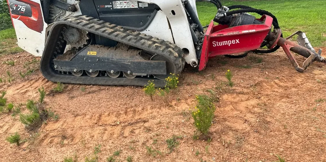Tracked skid steer with a stump grinding attachment on red clay near Shelby, NC